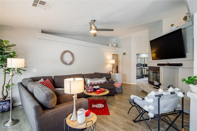 living area with wood finished floors, visible vents, ceiling fan, vaulted ceiling, and a glass covered fireplace