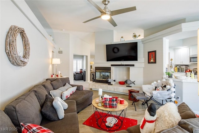 living area with a tiled fireplace, a ceiling fan, and wood finished floors