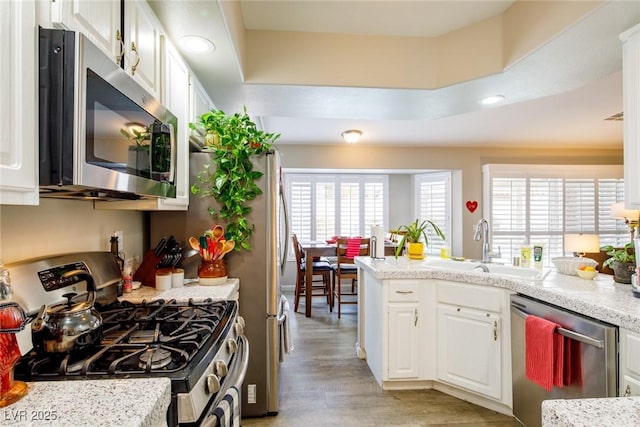 kitchen with a sink, white cabinetry, stainless steel appliances, a peninsula, and light wood finished floors