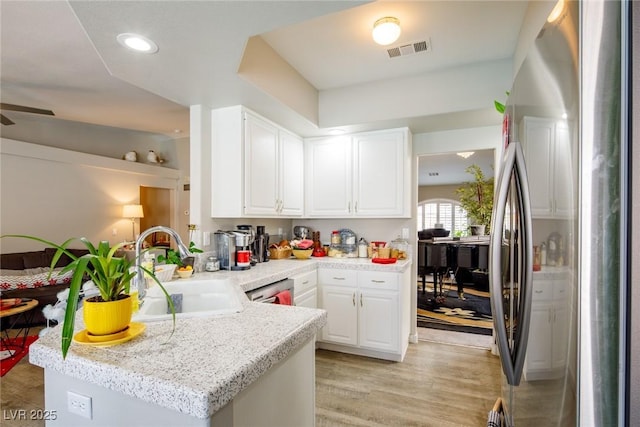 kitchen with visible vents, a sink, freestanding refrigerator, a peninsula, and white cabinets