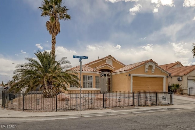 mediterranean / spanish home featuring stucco siding, driveway, a tile roof, a fenced front yard, and an attached garage