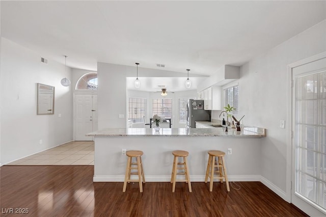 kitchen featuring visible vents, a kitchen bar, a peninsula, freestanding refrigerator, and wood finished floors