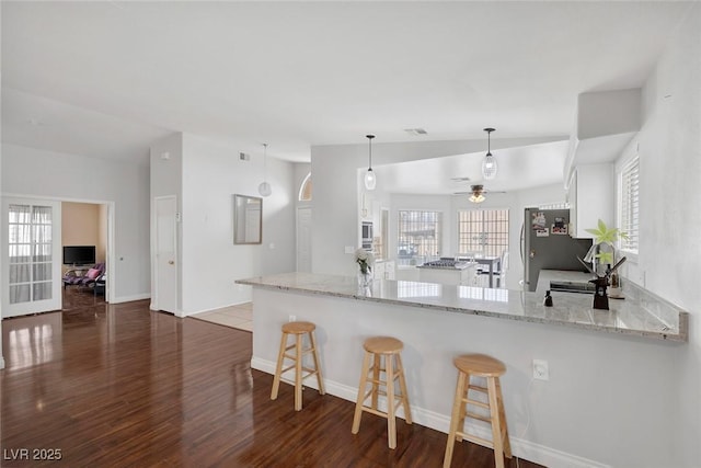 kitchen with a breakfast bar area, light stone countertops, a peninsula, dark wood-type flooring, and vaulted ceiling