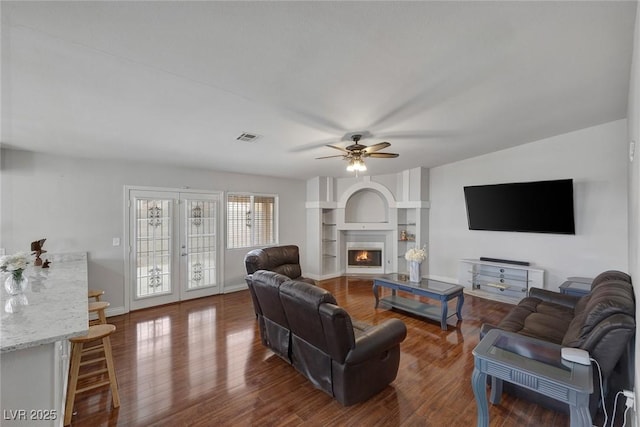 living room featuring visible vents, baseboards, a warm lit fireplace, and dark wood finished floors