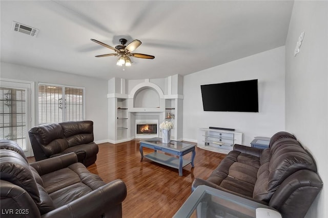 living room with visible vents, wood finished floors, a lit fireplace, baseboards, and ceiling fan