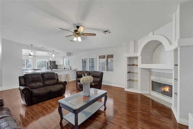 living room with built in features, baseboards, wood finished floors, and a tiled fireplace