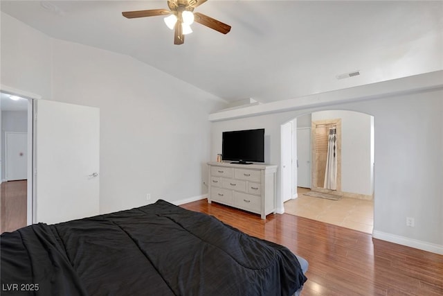 bedroom with arched walkways, visible vents, lofted ceiling, and wood finished floors