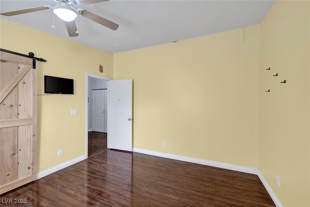 unfurnished bedroom with a ceiling fan, a barn door, wood finished floors, and baseboards