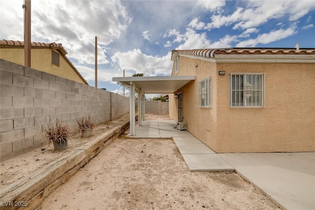 view of side of home featuring stucco siding, a fenced backyard, and a tiled roof