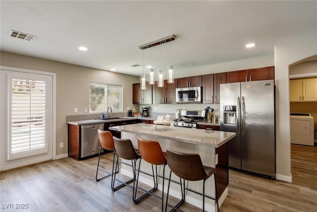 kitchen with visible vents, a kitchen island, washer / clothes dryer, a sink, and appliances with stainless steel finishes