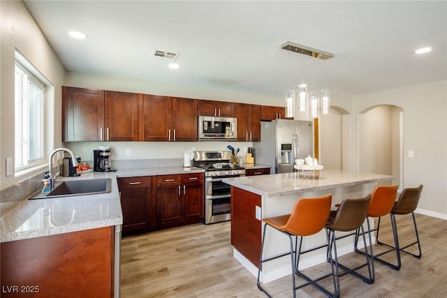 kitchen with a sink, light wood-style floors, appliances with stainless steel finishes, a kitchen bar, and a center island