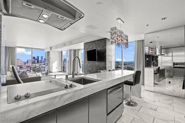 kitchen featuring open floor plan, marble finish floor, modern cabinets, wall chimney exhaust hood, and a sink