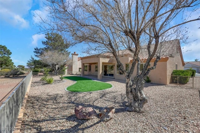 rear view of property featuring a patio area, stucco siding, a chimney, and fence