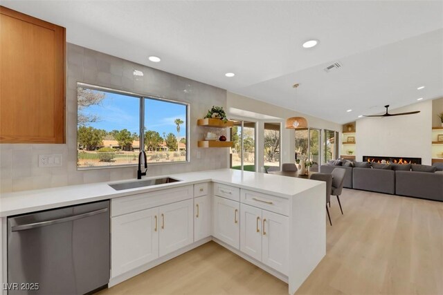 kitchen with visible vents, light countertops, a warm lit fireplace, stainless steel dishwasher, and a sink