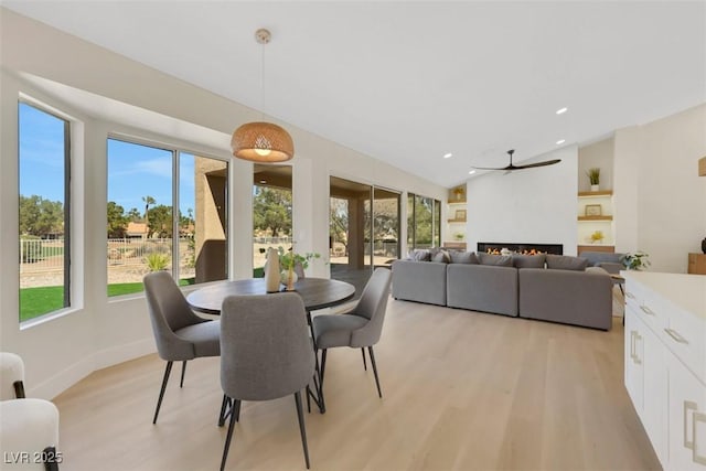 dining space featuring light wood-type flooring, recessed lighting, baseboards, a lit fireplace, and lofted ceiling