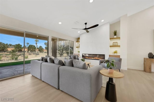 living room with a glass covered fireplace, vaulted ceiling, light wood-style floors, and a ceiling fan