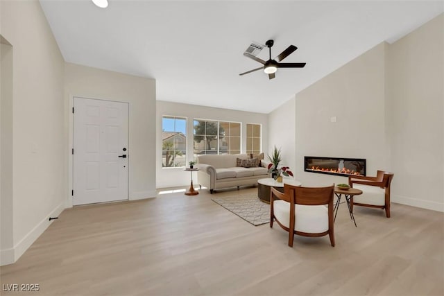 living area with a glass covered fireplace, light wood-style flooring, baseboards, and visible vents