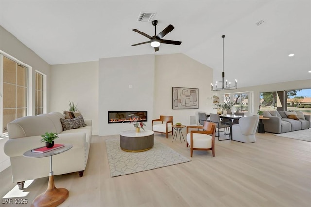 living room featuring a glass covered fireplace, vaulted ceiling, wood finished floors, and visible vents