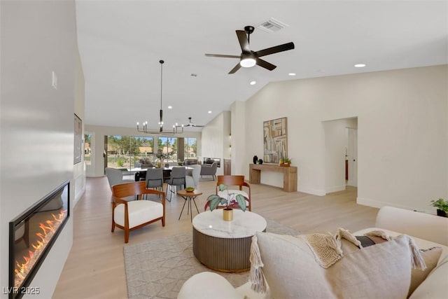 living area with visible vents, light wood finished floors, high vaulted ceiling, a glass covered fireplace, and ceiling fan with notable chandelier