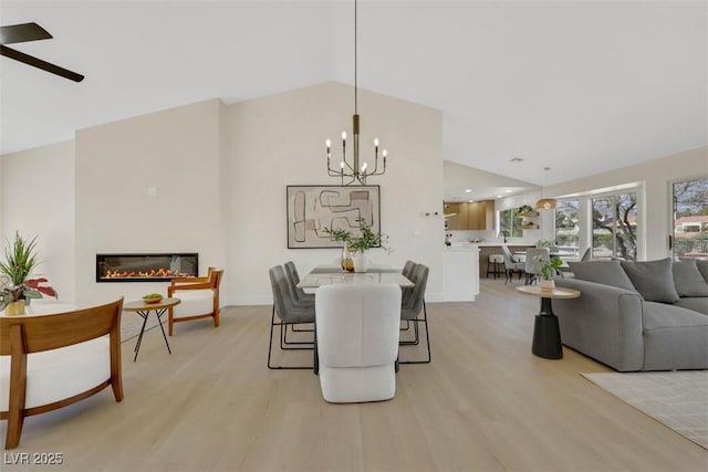 dining area featuring light wood finished floors, a notable chandelier, a glass covered fireplace, and vaulted ceiling