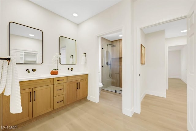 bathroom with wood finished floors, double vanity, a stall shower, a sink, and toilet