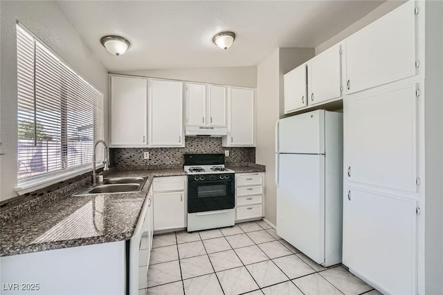 kitchen with dark countertops, freestanding refrigerator, a sink, under cabinet range hood, and gas range