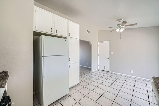 kitchen featuring visible vents, a ceiling fan, freestanding refrigerator, arched walkways, and white cabinets