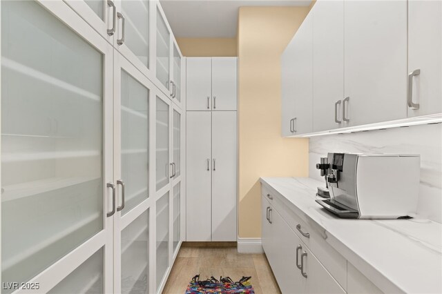 kitchen with white cabinets, light stone counters, glass insert cabinets, and light wood-type flooring