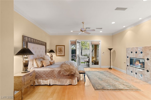 bedroom featuring baseboards, ornamental molding, wood-type flooring, a tiled fireplace, and access to outside