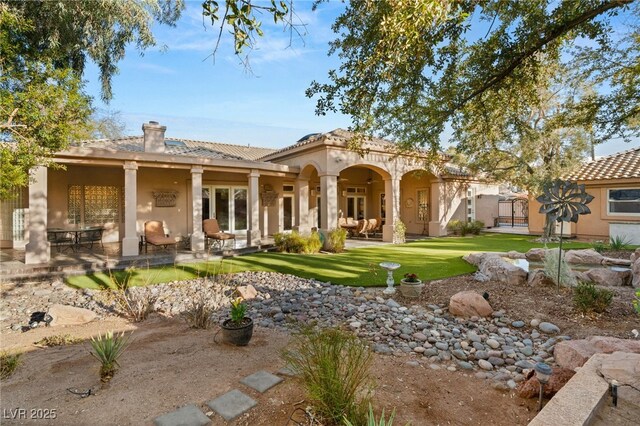 back of property with a tiled roof, stucco siding, a lawn, a chimney, and a patio area