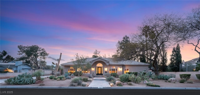 view of front of property featuring a tiled roof, stucco siding, and fence