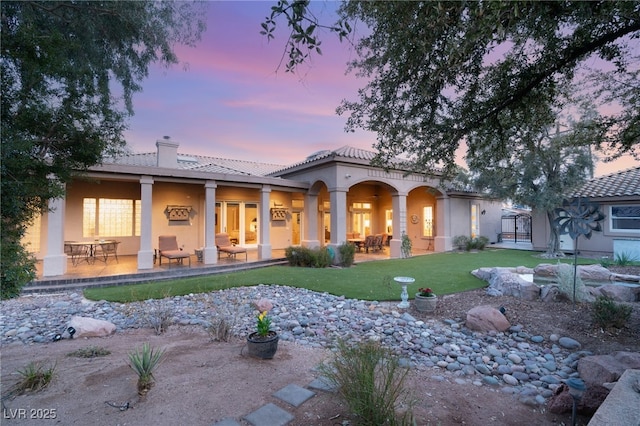 back of property featuring a yard, stucco siding, a chimney, a tile roof, and a patio area