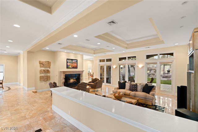 living area with visible vents, crown molding, baseboards, a tray ceiling, and a glass covered fireplace