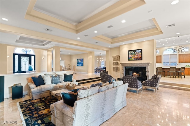 living area featuring visible vents, ornamental molding, a premium fireplace, a raised ceiling, and a chandelier