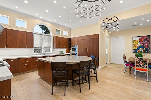 kitchen featuring a sink, visible vents, an island with sink, and crown molding