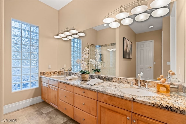 bathroom with double vanity, a stall shower, baseboards, and a sink