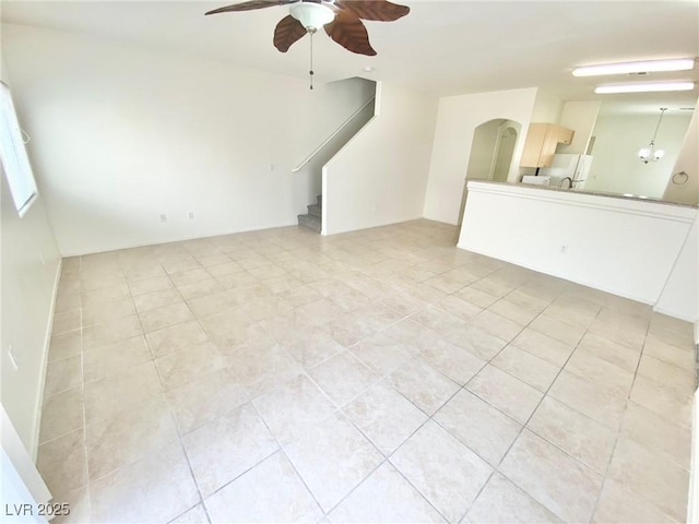 unfurnished living room featuring arched walkways, ceiling fan with notable chandelier, stairs, and light tile patterned flooring