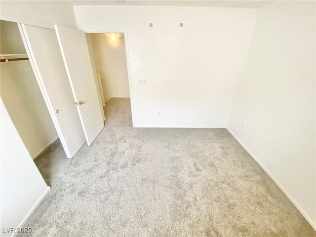 unfurnished bedroom with a closet, carpet flooring, attic access, and baseboards