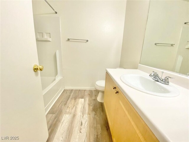 bathroom featuring baseboards, toilet, vanity, wood finished floors, and washtub / shower combination