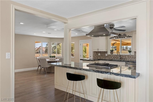 kitchen featuring dark wood finished floors, decorative backsplash, appliances with stainless steel finishes, wall chimney exhaust hood, and a sink