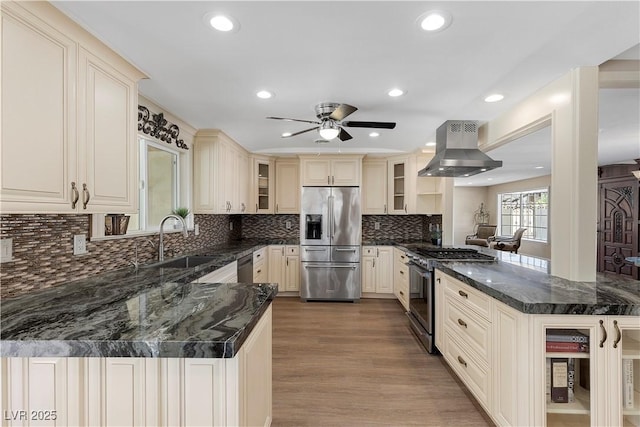 kitchen with appliances with stainless steel finishes, island exhaust hood, a peninsula, cream cabinetry, and a sink