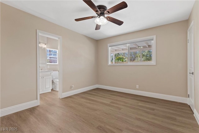 unfurnished bedroom featuring multiple windows, light wood-style floors, baseboards, and ensuite bathroom