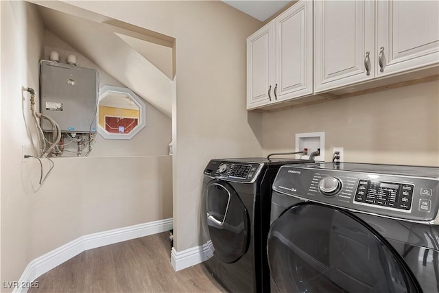 laundry room featuring light wood finished floors, baseboards, washer and clothes dryer, tankless water heater, and cabinet space