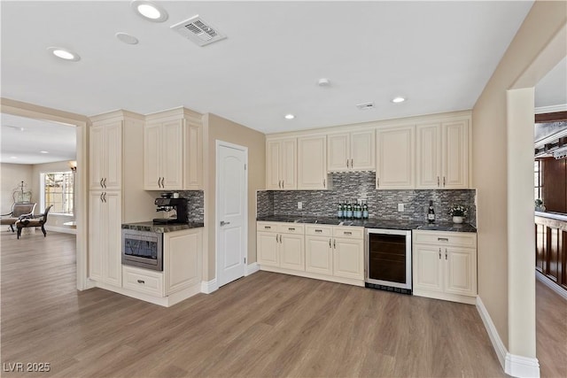 kitchen featuring visible vents, light wood-style flooring, stainless steel microwave, cream cabinets, and wine cooler