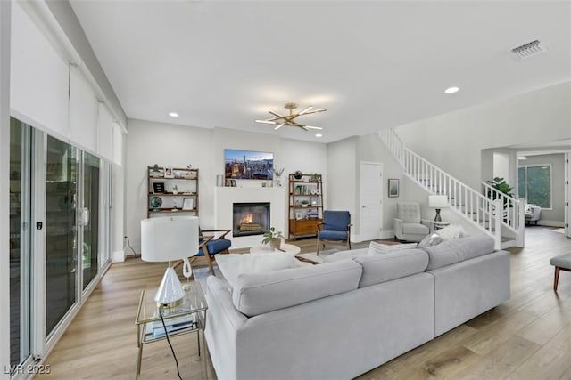 living area featuring a glass covered fireplace, stairs, recessed lighting, and light wood-type flooring