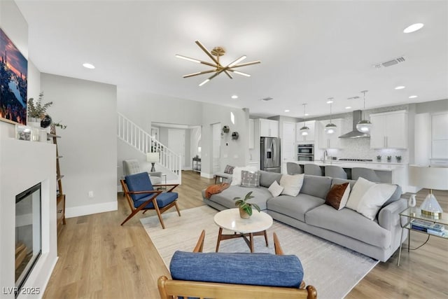 living room with visible vents, stairs, recessed lighting, light wood-style floors, and a glass covered fireplace