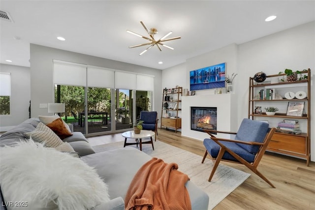 living area featuring wood finished floors, visible vents, recessed lighting, a glass covered fireplace, and a chandelier