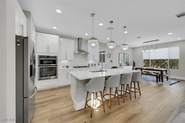 kitchen with visible vents, backsplash, stainless steel appliances, wall chimney exhaust hood, and a sink