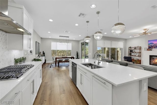 kitchen with visible vents, a sink, wall chimney range hood, stainless steel appliances, and light countertops