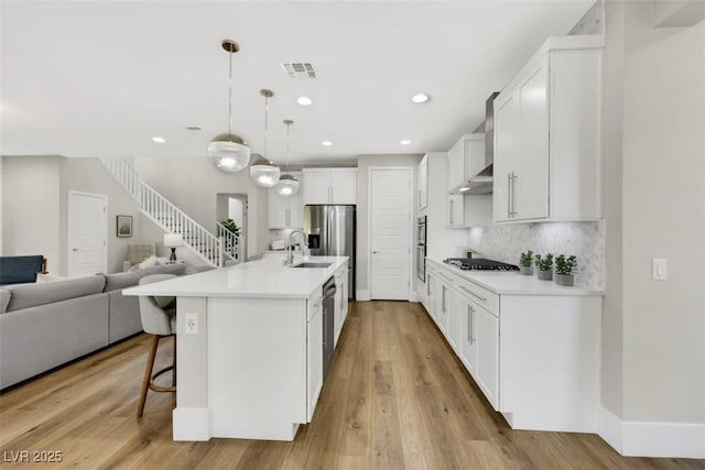 kitchen with visible vents, a kitchen bar, a sink, open floor plan, and wall chimney range hood